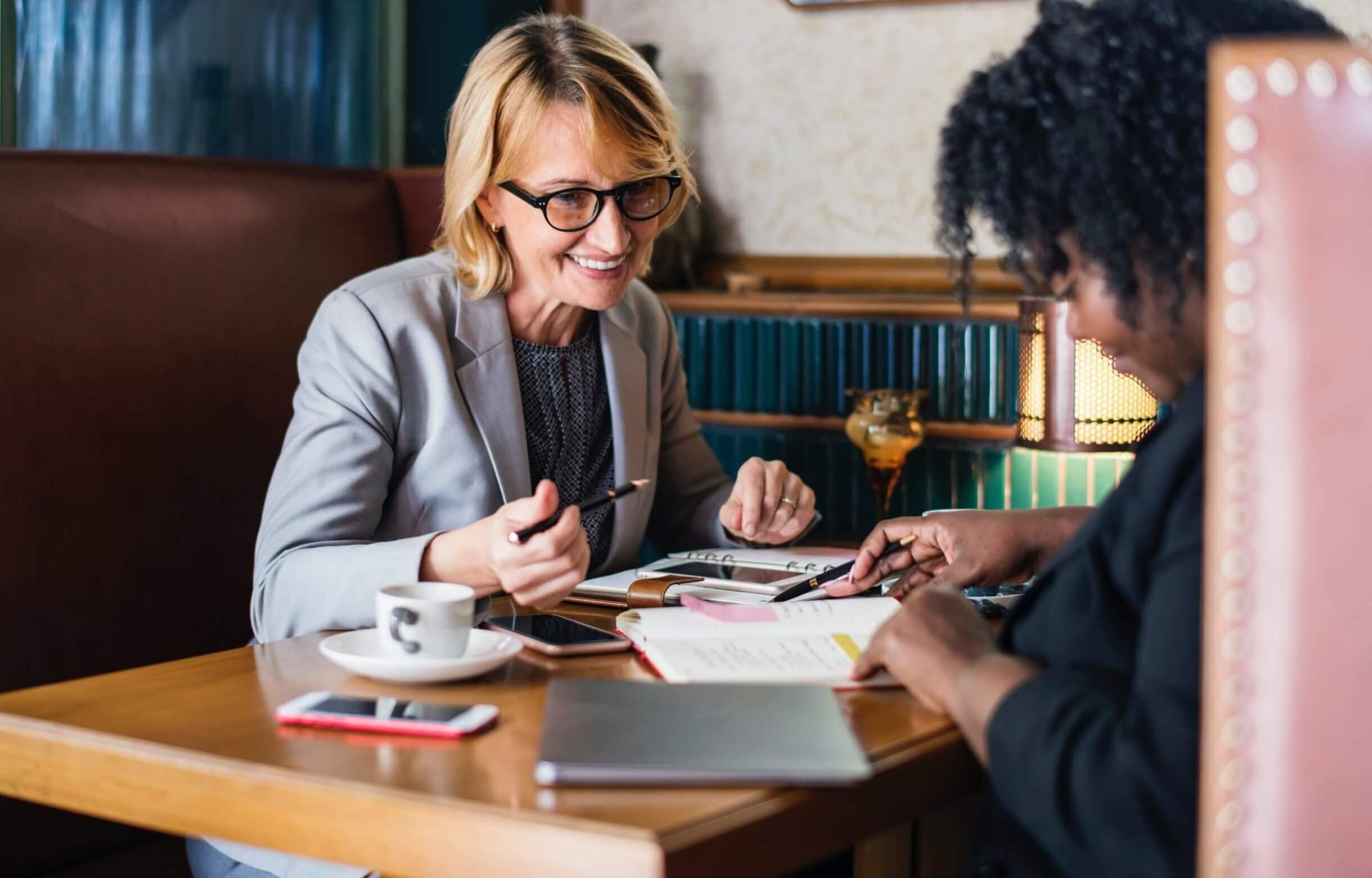 Employee engagement strategies concept featuring two women meeting in a booth happy workers