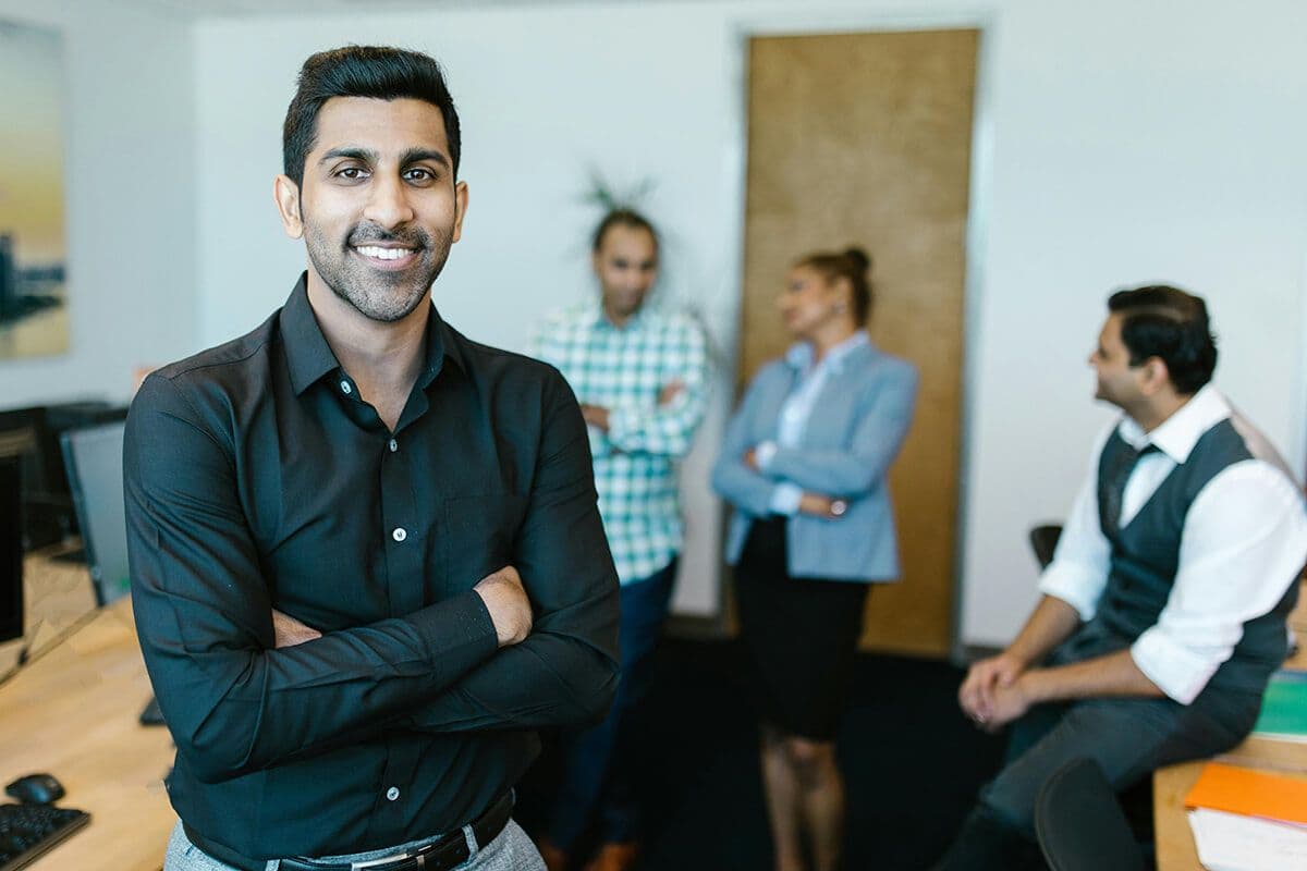 man smiling standing in a conference room with other colleagues discussing the leadership styles of their company