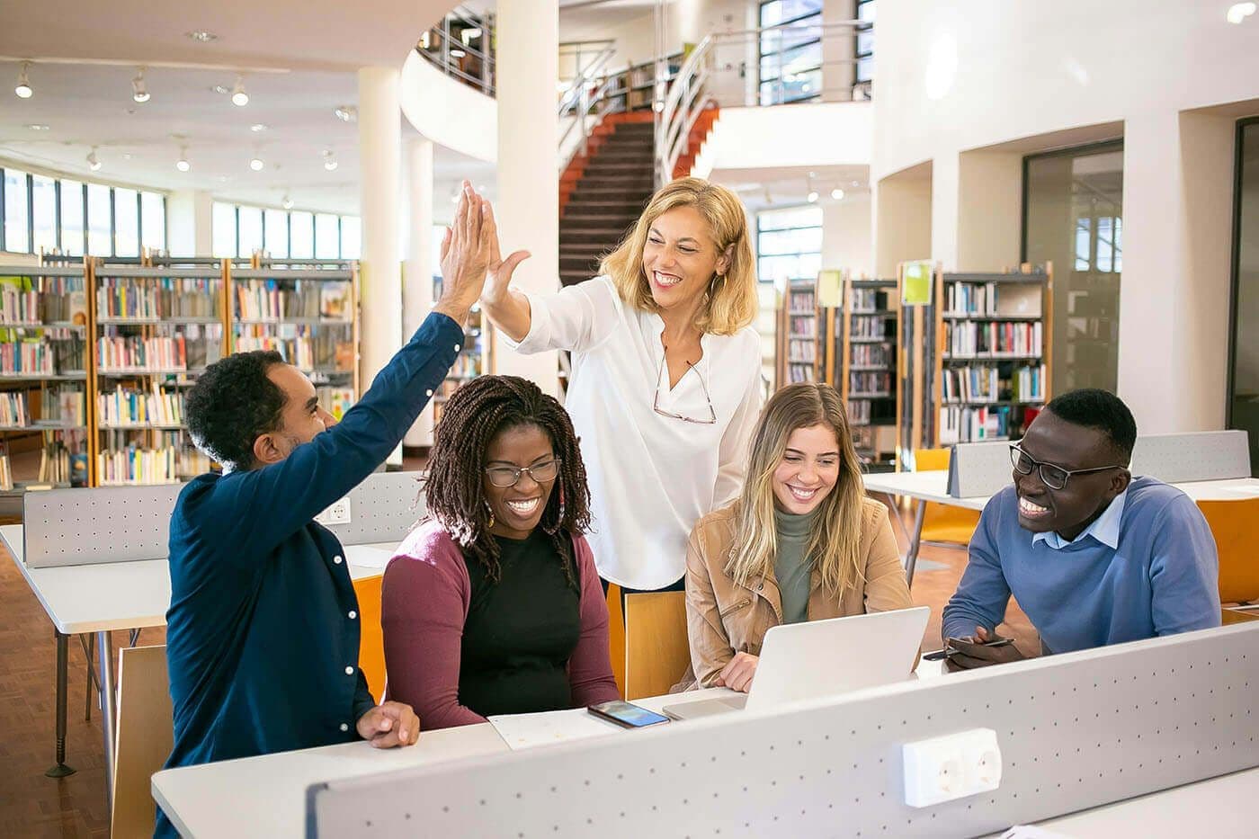 A team high-fives around a table in a bright library