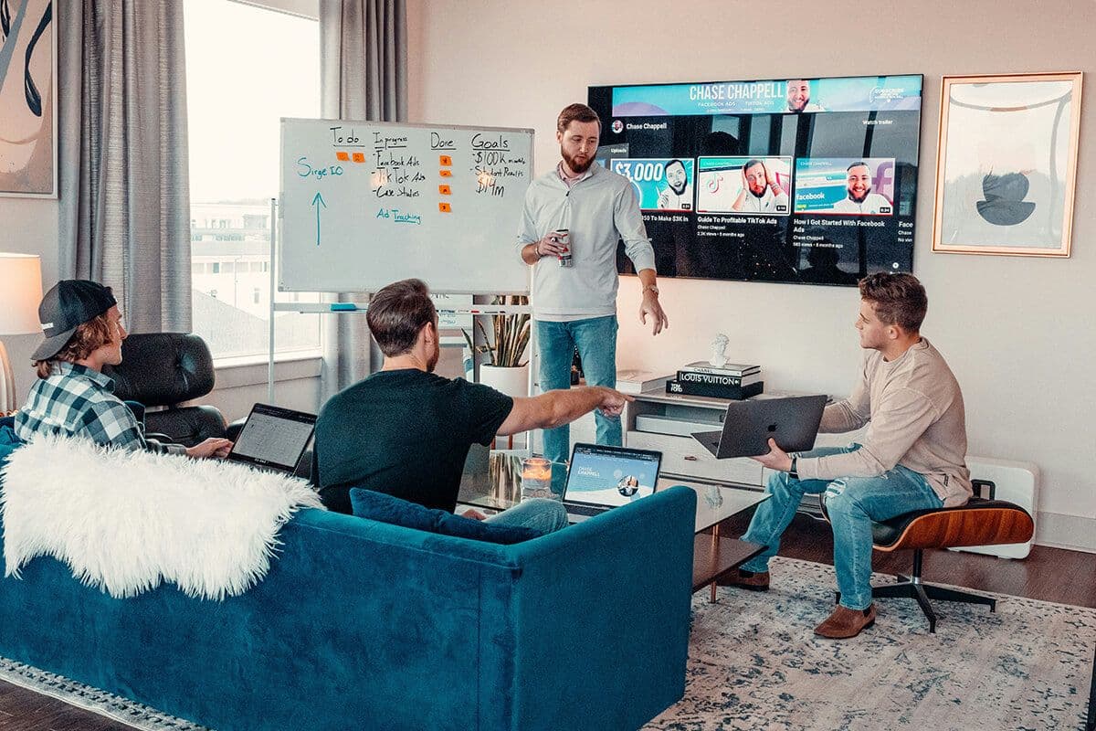 Four male colleagues sitting in a conference room in front of a tv and a whiteboard. They're in an upskilling social learning session.