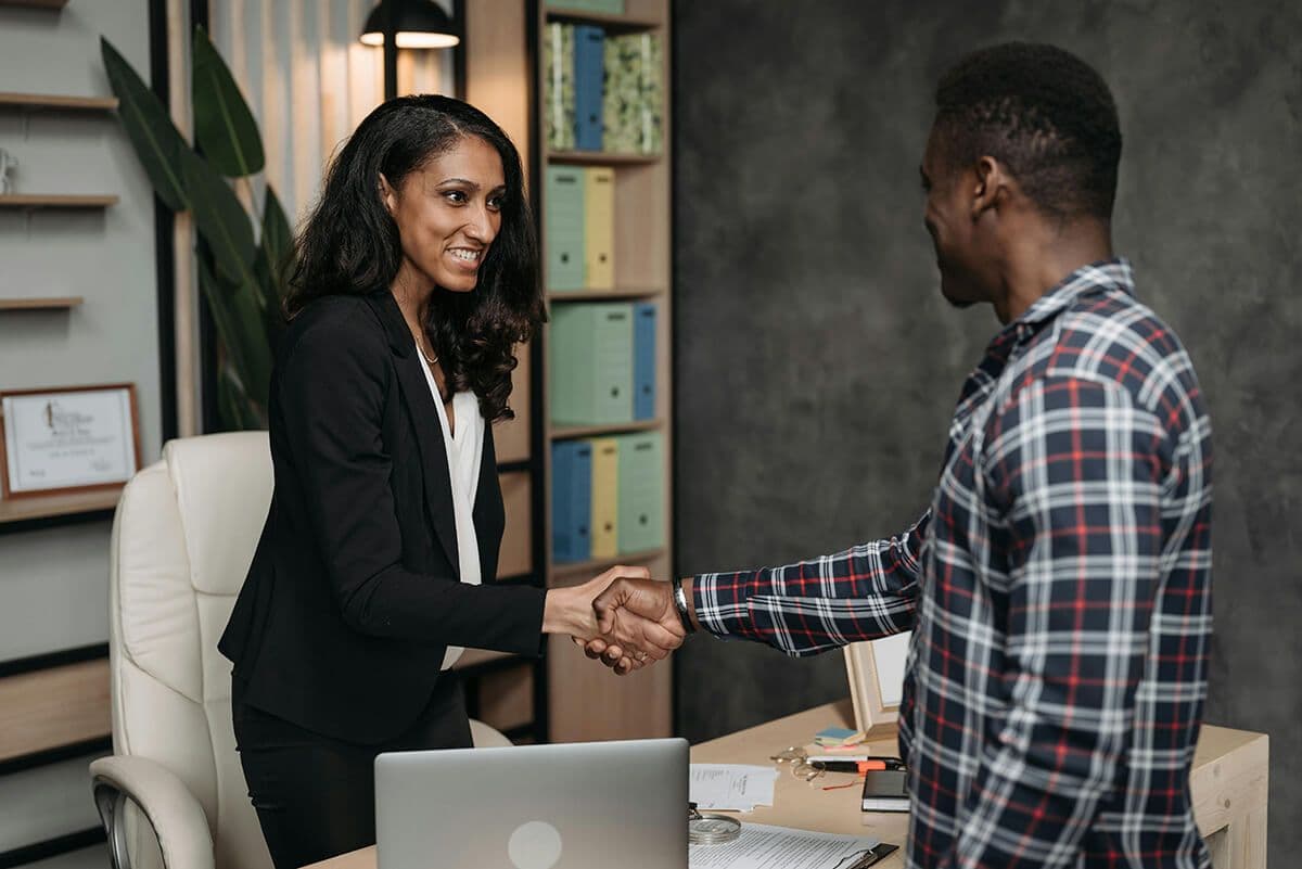 Woman employee shaking hands with male direct report in an office across her desk.