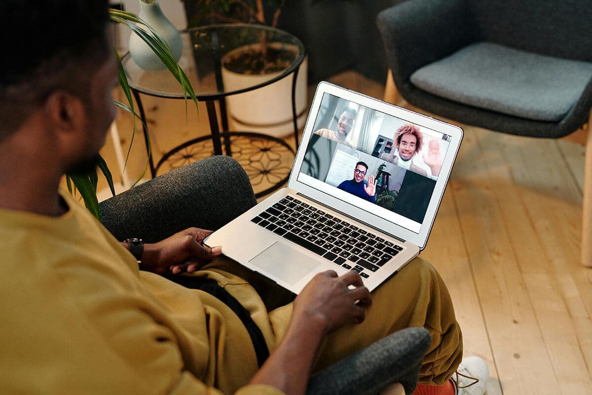 Remote male employee sitting in a chair with a laptop, looking at a video call with three other colleagues